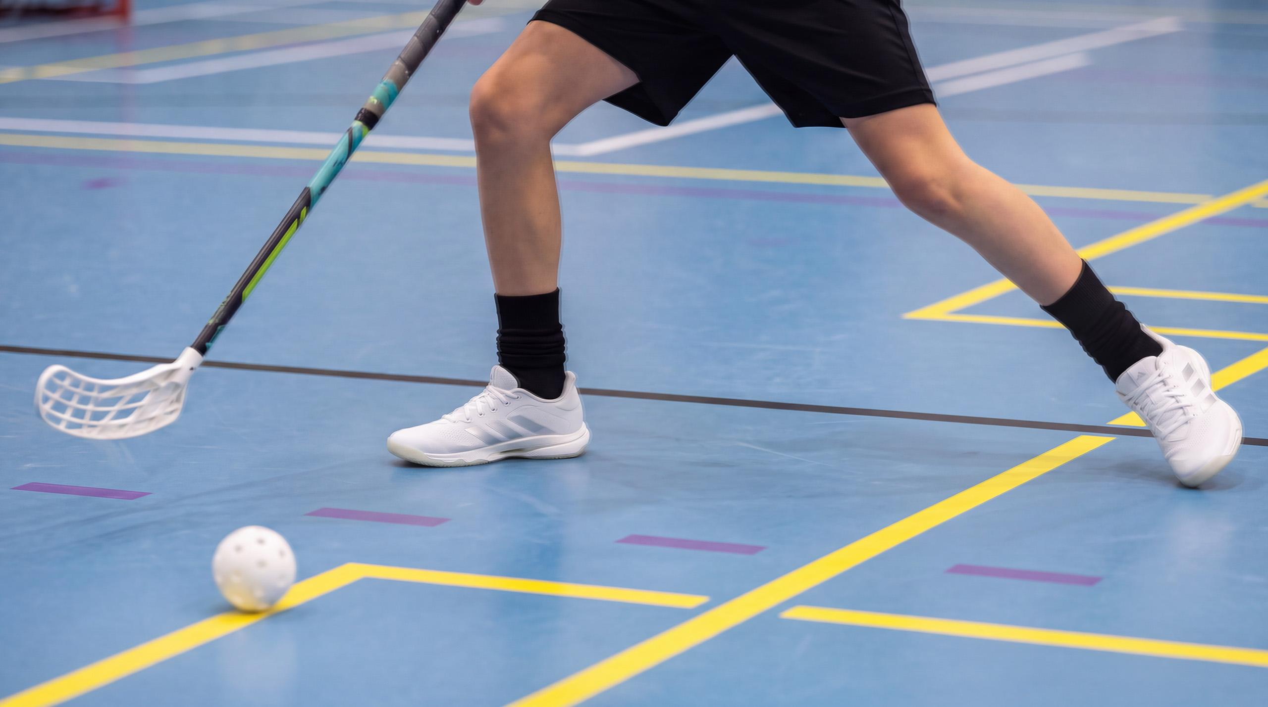 Innebandyspelare med klubba och boll på en inomhusplan